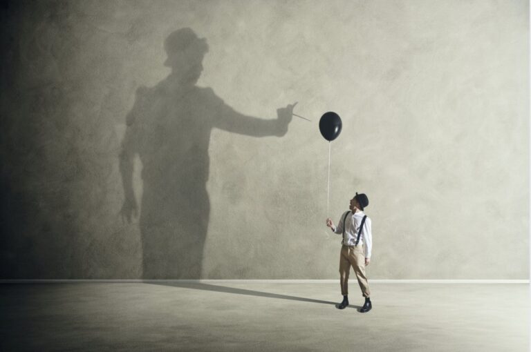 Ein kleiner Junge hält einen schwarzen Luftballon, an der Wand hinter ihm der große Schatten eines Mannes, der mit einer Nadel nach dem Ballon greift