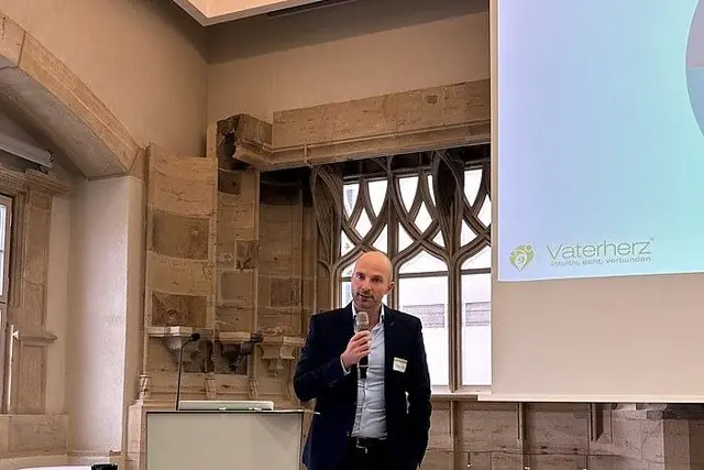 Carsten Vonnoh hält einen Fachvortrag in einem historischen Saal, auf der Leinwand das Vaterherz®-Logo
