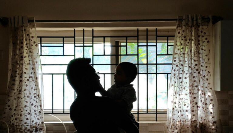 Vater hält sein Kind am Abend in der Küche, Silhouette vor dem Fenster