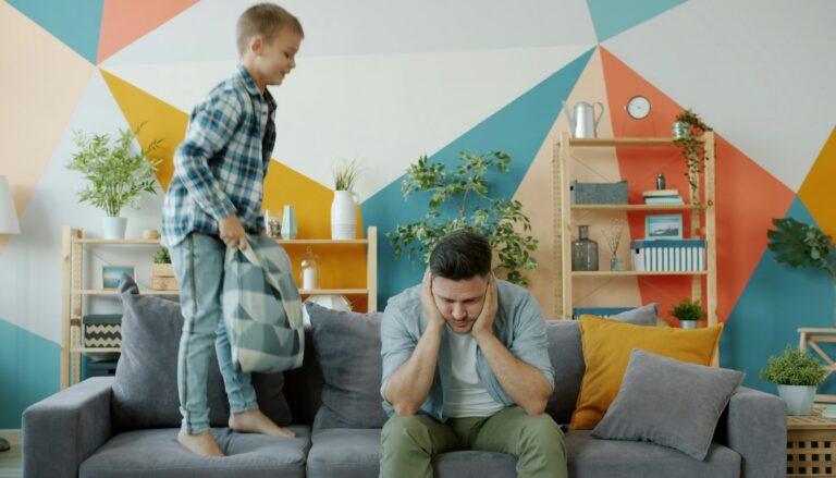 Vater sitzt erschöpft da, während sein Sohn auf der Couch springt