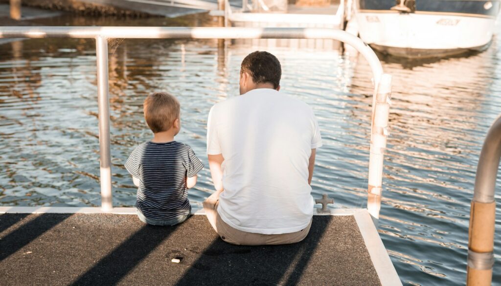 Vater und Sohn sitzen nebeneinander auf einem Holzsteg am Wasser