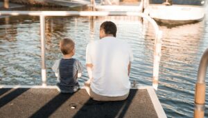 Vater und Sohn sitzen nebeneinander auf einem Holzsteg am Wasser