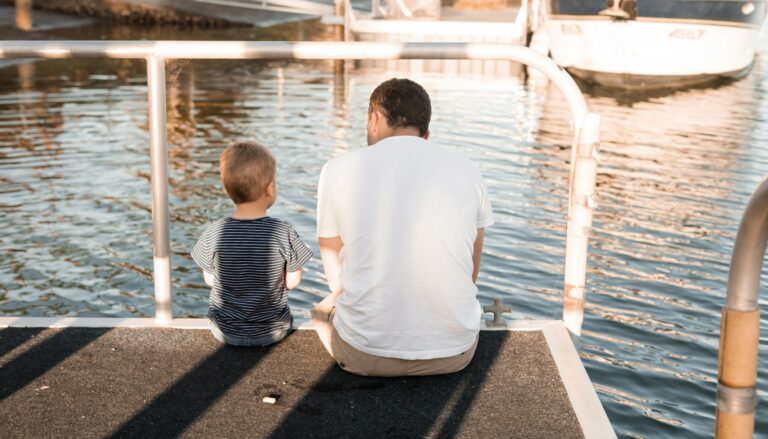 Vater und Sohn sitzen nebeneinander auf einem Holzsteg am Wasser